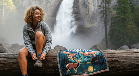 Woman sitting on a log with a Yosemite blanket featuring a deer design, waterfall in the background