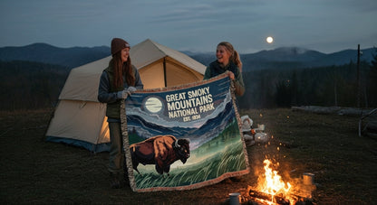 Two people holding a Great Smoky Mountains National Park blanket by a campfire at night.