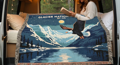 Person holding a book next to a decorative blanket with a mountain and eagle design, inside a vehicle.