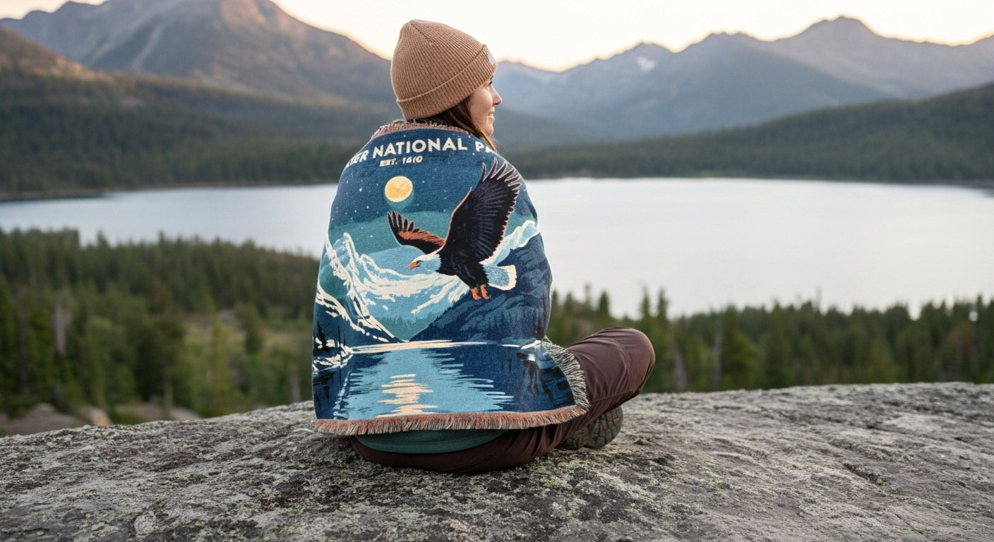 Person sitting on a rock by a lake wearing a National Park Foundation blanket